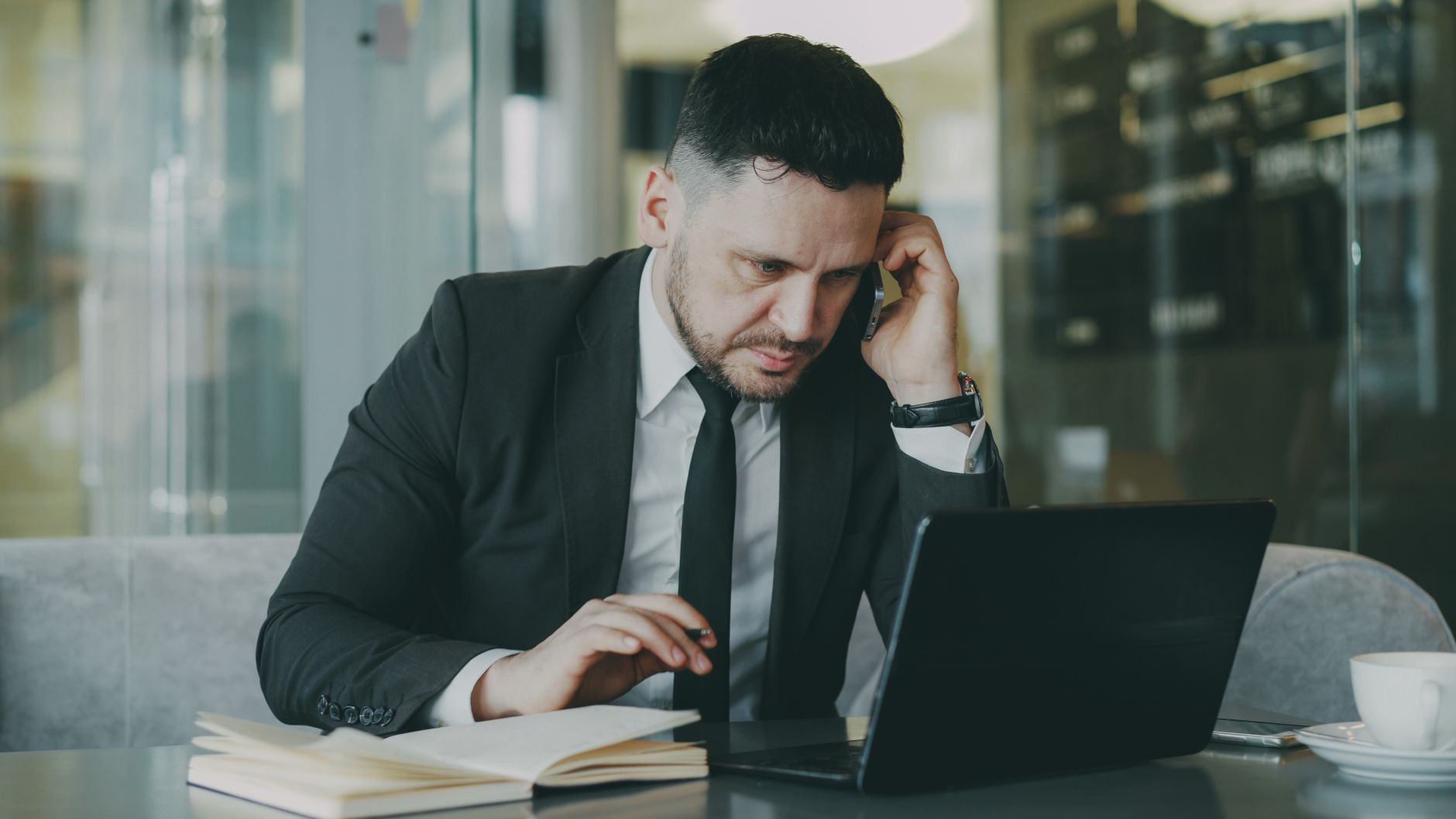 Focused businessman in suit multitasking on phone and laptop in modern office. — Buy Coffee Online- How Coffee Can Help You S
