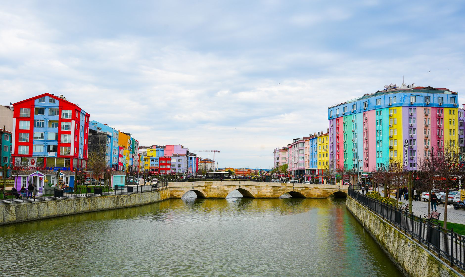 Vibrant cityscape with colorful buildings along a river and stone bridge under a cloudy sky. — BuyTikTok Followers: Trending