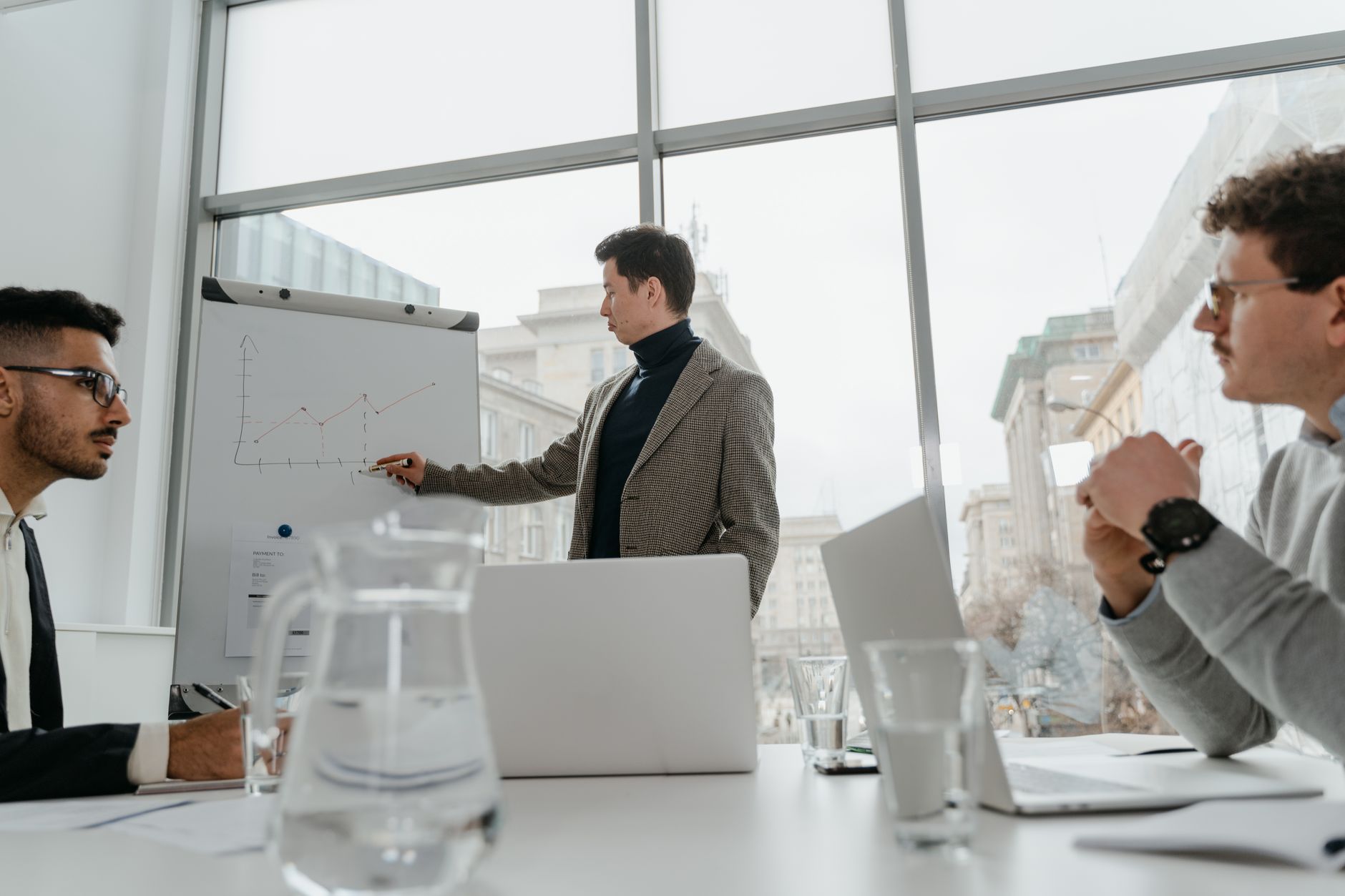 Professionals engaged in a collaborative business meeting with charts and laptops in a modern office setting. — Crucial Benef
