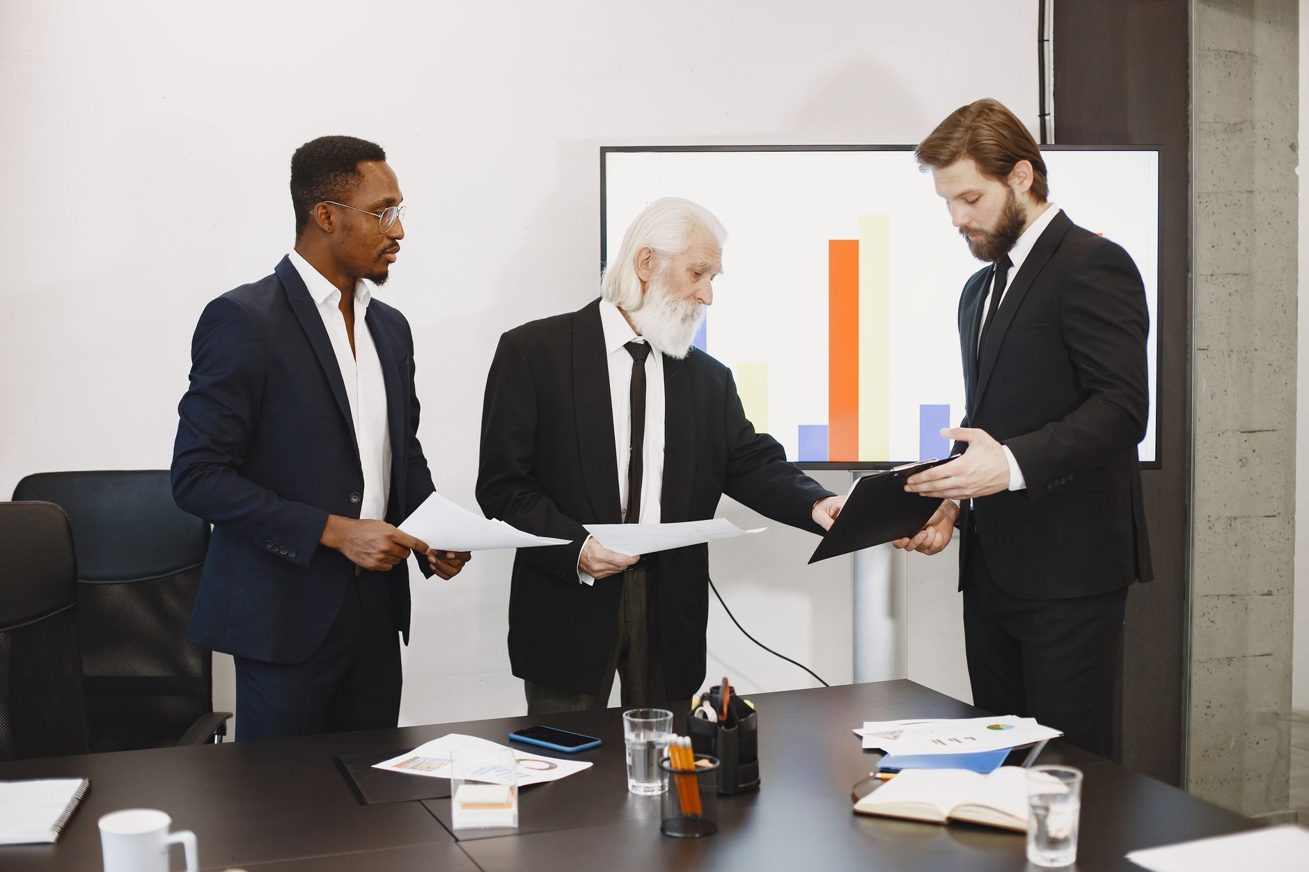 Three businessmen discussing documents in a conference setting with a presentation screen. — How to Stay Connected With Your