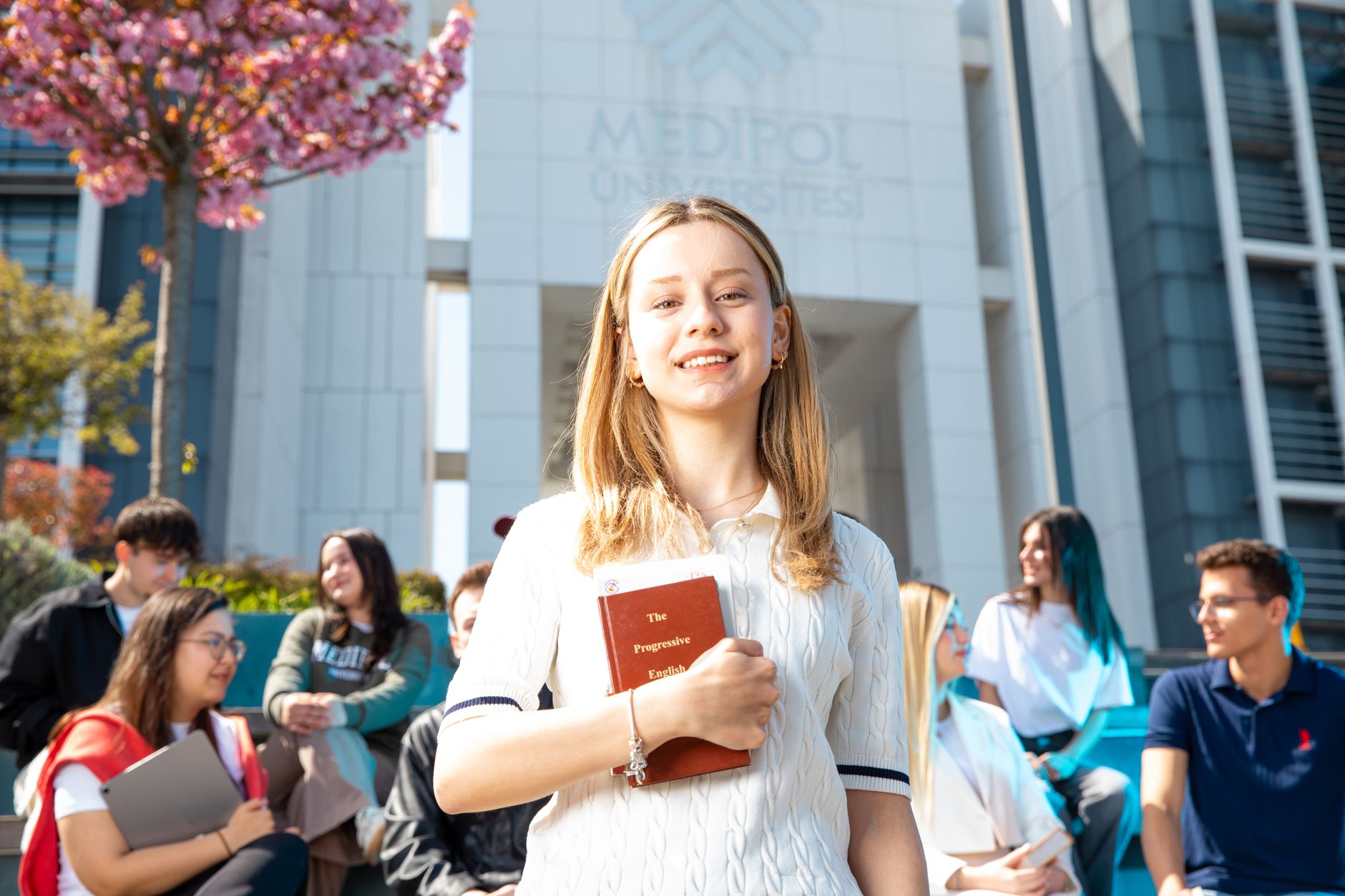 Happy university students socializing on campus, with a focus on a smiling young woman holding a book. — Where are some other